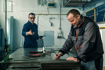 Two factory workers collaborating while measuring metal sheeting on a workbench