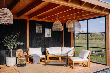 Stylish outdoor lounge with wooden furniture, rattan pendant lights, potted plants, and soft...