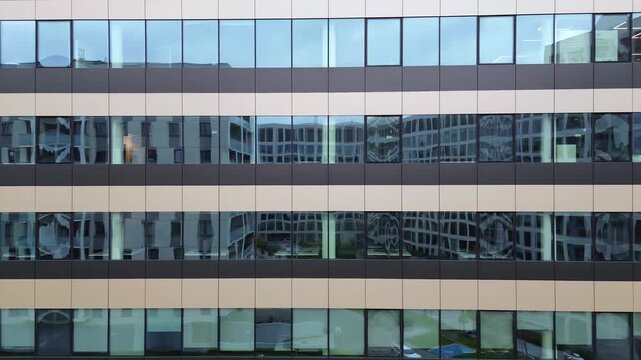 Modern office building exterior showcasing sleek glass facade, camera pans across reflective windows revealing urban surroundings and architectural details, emphasizing contemporary design elements