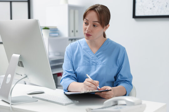 Nurse with clipboard working at desk in office