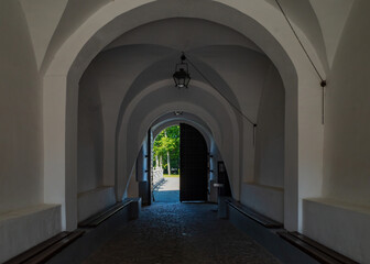Arched hallway with benches in Nesvizh Castle with natural light from an open exit.