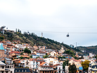 Scenic view of Tbilisi Old Town, Georgia, with colorful houses, historic churches, cable cars, and Mother of Georgia statue on the hill, capturing cultural charm and layered city heritage.