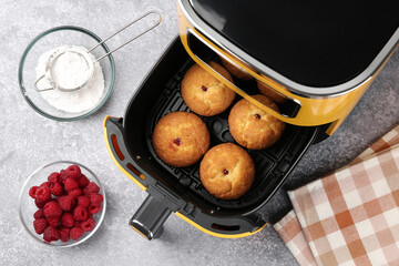 Freshly baked muffins in air fryer and ingredients on grey textured table, flat lay