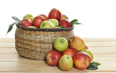 Fresh apples in wicker basket and green leaves on wooden table against white background