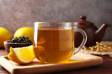 Aromatic tea in cup with lemons and dry leaves on wooden table, closeup