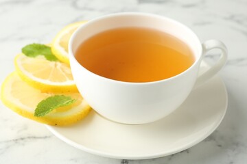 Aromatic tea in cup with lemon and mint on white marble table, closeup