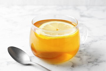 Aromatic tea with lemon in cup and spoon on white marble table, closeup