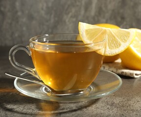 Aromatic tea in cup with lemons and spoon on grey table, closeup