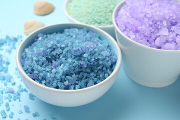 Different types of sea salt on light blue background, closeup