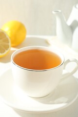 Aromatic tea in cup, lemons and teapot on white table, closeup