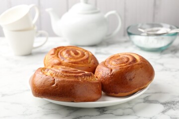 Tasty roll buns, cups, teapot and flour on white marble table, closeup