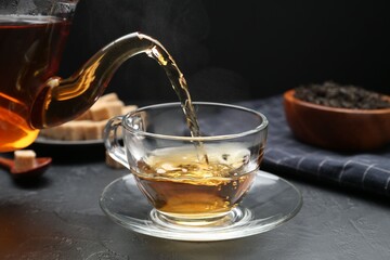 Pouring aromatic tea into glass cup at black table, closeup