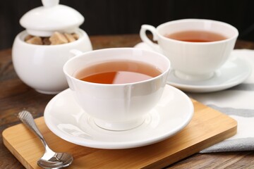 Aromatic black tea in cups and brown sugar on wooden table, closeup