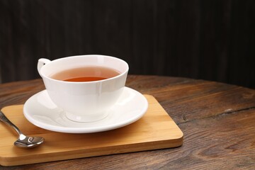 Aromatic black tea in cup and spoon on wooden table, closeup. Space for text