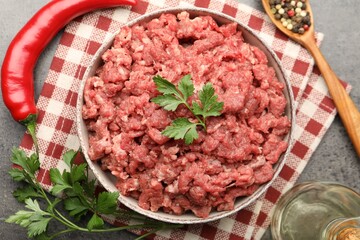 Raw minced meat with parsley and spices on grey table, flat lay