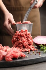 Woman making minced meat with grinder at grey table, closeup