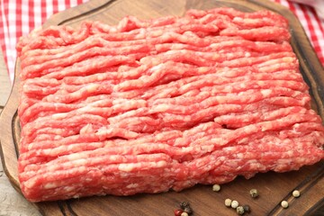 Raw minced meat and peppercorns on wooden table, closeup