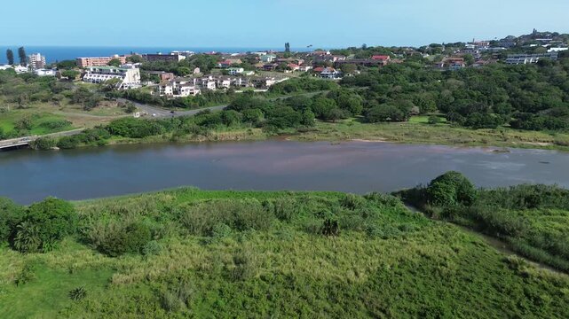 Camera pushing in towards the coastal town of Scottburgh over green rolling hills and a river on the South Coast of KwaZulu-Natal, Aerial 4K video.