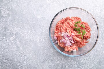 Raw minced meat with onion and parsley in bowl on grey table, top view. Space for text