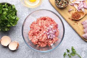 Raw minced meat with onion, parsley, spices and egg on grey table, flat lay