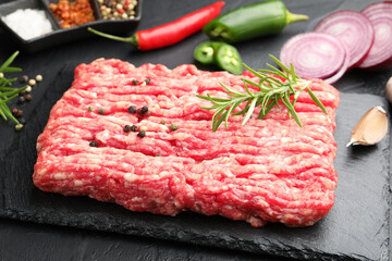 Raw minced meat with rosemary, spices, onion and chili peppers on black table, closeup