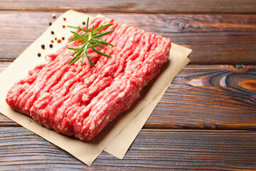 Raw minced meat with peppercorns and rosemary on wooden table, closeup. Space for text
