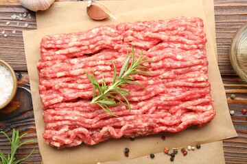 Raw minced meat with rosemary and spices on wooden table, flat lay