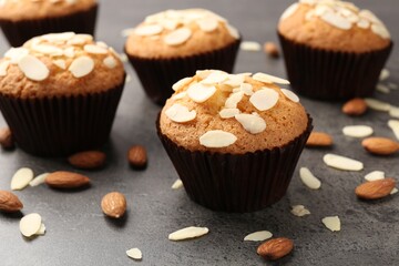 Tasty muffins with almond flakes and nuts on grey table, closeup