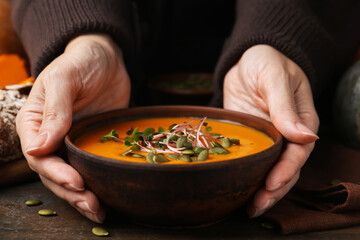 Woman with delicious pumpkin soup at wooden table, closeup