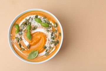 Delicious pumpkin soup with spices, cheese and sour cream in bowl on beige table, top view. Space for text