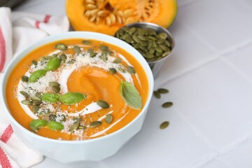 Delicious pumpkin soup with spices, cheese and sour cream in bowl on white tiled table, closeup. Space for text