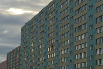 Long row of apartment blocks under cloudy sky, showcasing repetitive architecture, urban density, and geometric symmetry of residential buildings