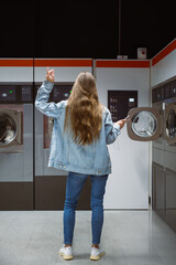 Woman dancing with smartphone in self service laundromat while waiting laundry