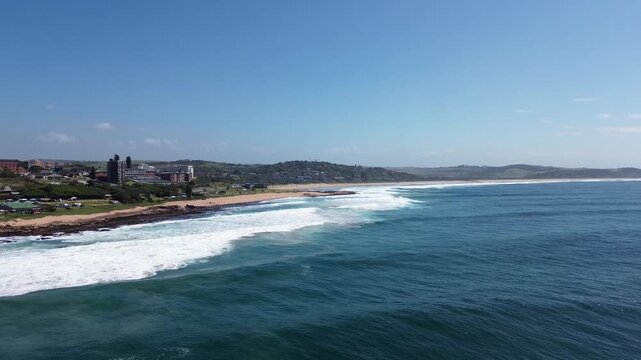 Camera rising up from the deep blue ocean over white waves, looking down the South Coast of KwaZulu-Natal to the coastal town of Scottburgh, Aerial 4K video.