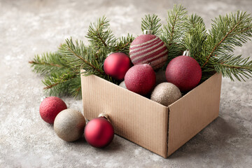 Christmas ornaments in a cardboard box with fir tree branches. Red and gold baubles for holiday decoration. Festive winter season still life.