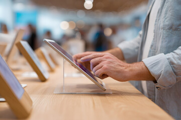 A customer examines a tablet in an electronics store. Close-up of a man's hands using the touchscreen. Modern retail and technology shopping