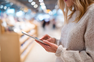 Woman using a tablet computer in a modern electronics store. Customer shopping for a new device during a sale. Consumerism and technology concept