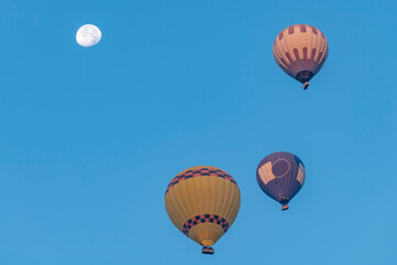 Three colorful hot air balloons in the sky with a nearly full moon in Pamukkale, Türkiye