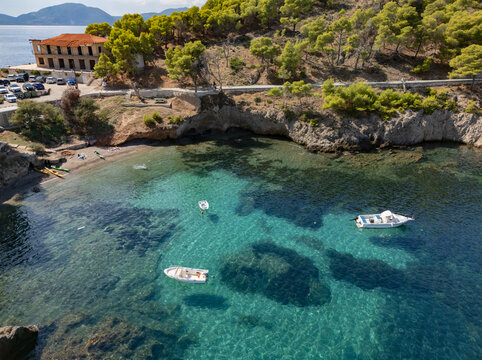 Aerial view of boats bobbing in the crystalline turquoise waters near the rugged coastline and historic building, Asos, Cephalonia, Greece.