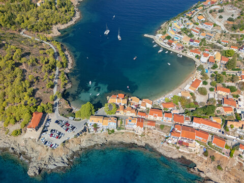 Aerial view of the quaint village nestled between the Ionian Sea and verdant hills, with turquoise waters contrasting against the red-tiled roofs of Asos, Cephalonia, Greece.