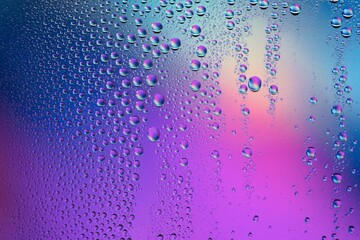 Vibrant iridescent water droplets shimmer on a gradient background creating a mesmerizing, abstract texture perfect for modern design backgrounds