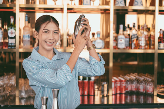 Smiling female bartender preparing a cocktail with a shaker behind the bar counter. bar staff working in a modern pub with bottles and beverages in the background. - Powered by Adobe
