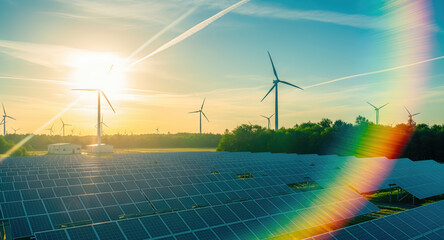 Solar panel array and wind turbines at renewable energy facility during sunset with rainbow light spectrum. Combined photovoltaic and power generation infrastructure, clean electricity production,