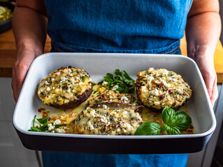 Woman holding baking dish with stuffed portobello mushrooms, close-up