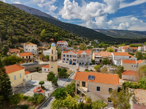 Aerial view of terracotta rooftops cascading towards the Ionian Sea, a church steeple piercing the skyline amidst verdant hills, Agia Effimia, Cephalonia, Greece.