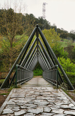 Modern metal bridge surrounded by lush trees, over the Duero River, in a forest setting, Soria,...