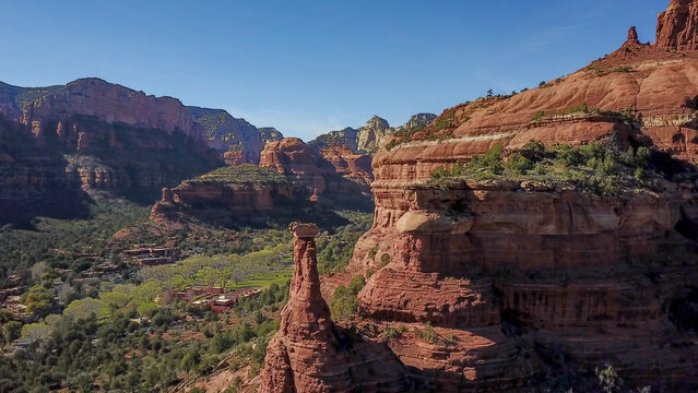 Aerial view of a towering rock formation jutting skyward amidst the rugged, sun-baked landscape of Sedona's red rock country, Arizona, United States.