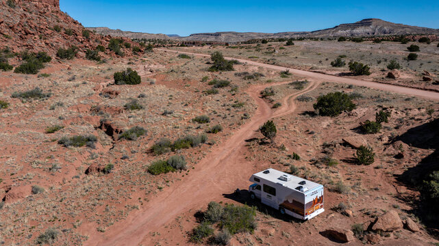 Aerial view of a recreational vehicle parked on a red dirt road amidst the rugged desert landscape under the vast blue sky, Sedona, Arizona, United States.