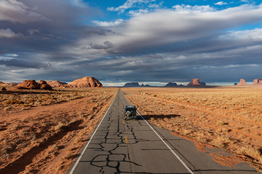 Aerial view of a lone car navigates the cracked asphalt through the arid landscape toward the iconic buttes and mesas, Sedona, Arizona, United States.