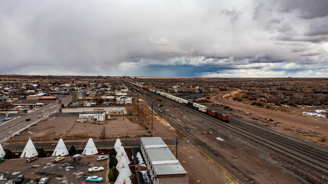 Aerial view of white teepees stand in stark contrast to the muted desert landscape under a dramatic sky, with a train cutting through the scene, Sedona, Arizona, United States.